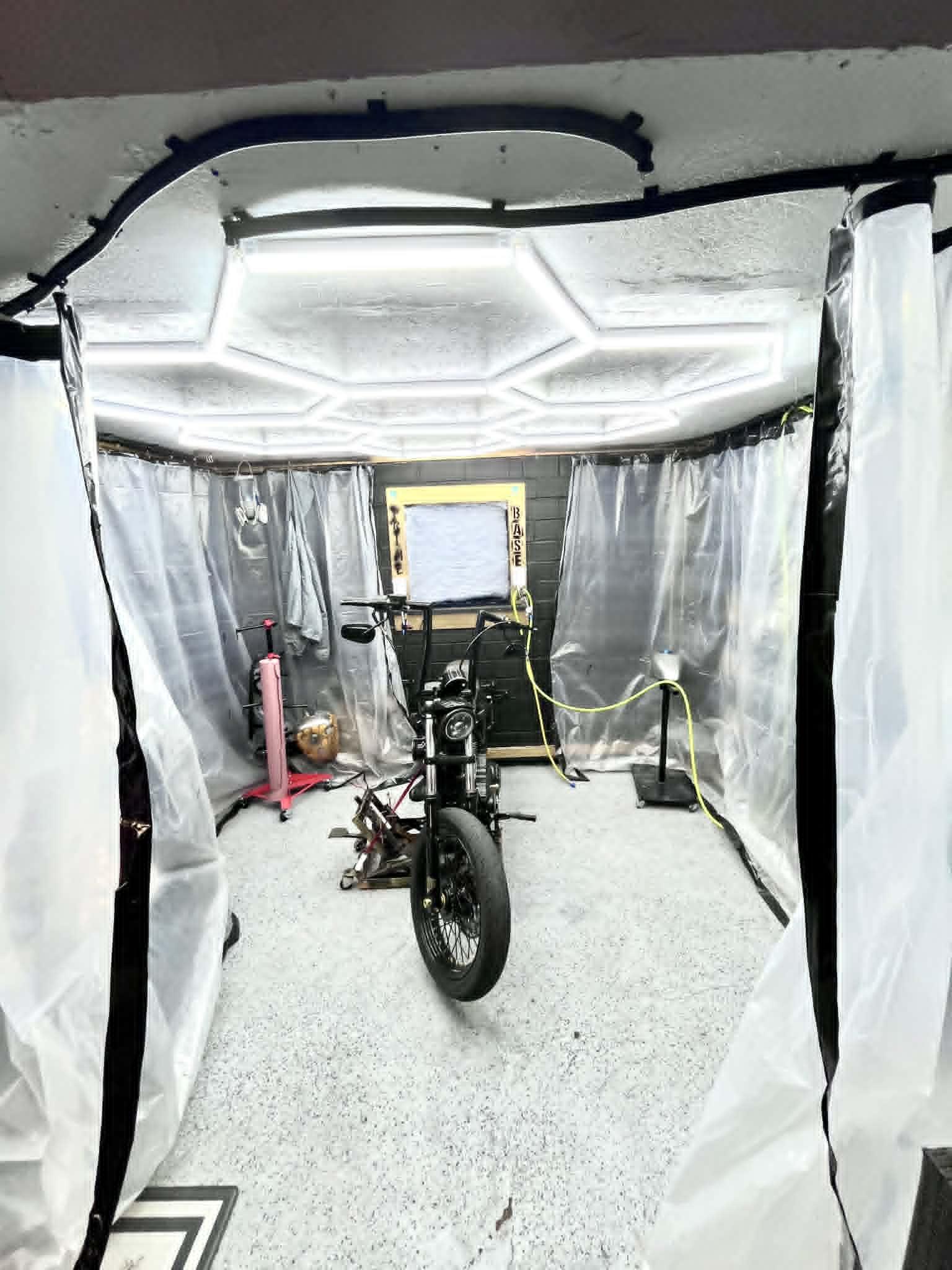 Iron Pony Customs paint booth — hex LED ceiling, clean plastic-curtain walls, bike staged inside the controlled environment